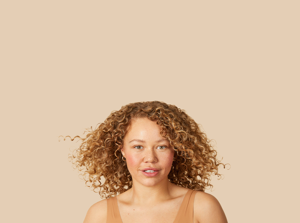 close-up van een vrouw met aardbei-blond krullend haar die naar de camera kijkt