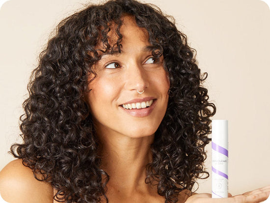 vrouw met donkerbruin krullend haar houdt een fles Bouclème's Protein Booster voor krullend haar vast