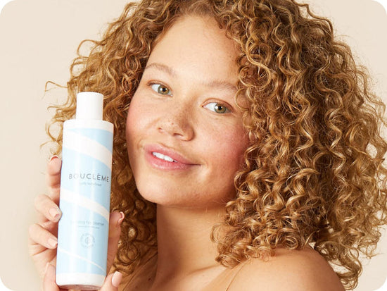 vrouw met aardbeienblond haar houdt een fles Bouclème Hydrating Hair Cleanser vast