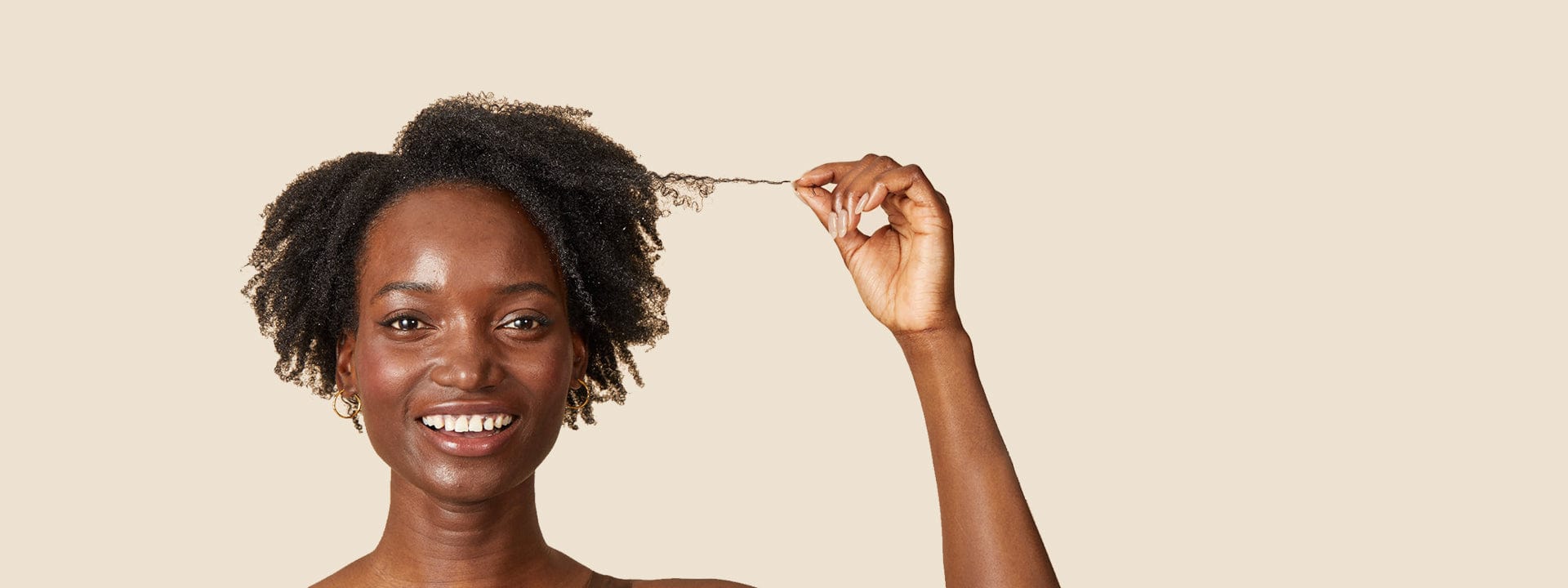 glimlachende, zwarte vrouw die een paar lokken van haar zwarte, warrige haar uitsteekt