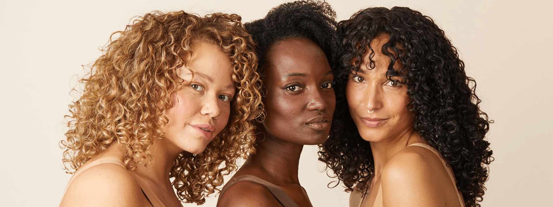 drie vrouwen met krullend haar staan dicht bij elkaar en kijken in de camera