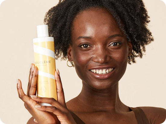 vrouw met zwart, kroeshaar houdt een fles Bouclème conditioner voor krullend haar vast